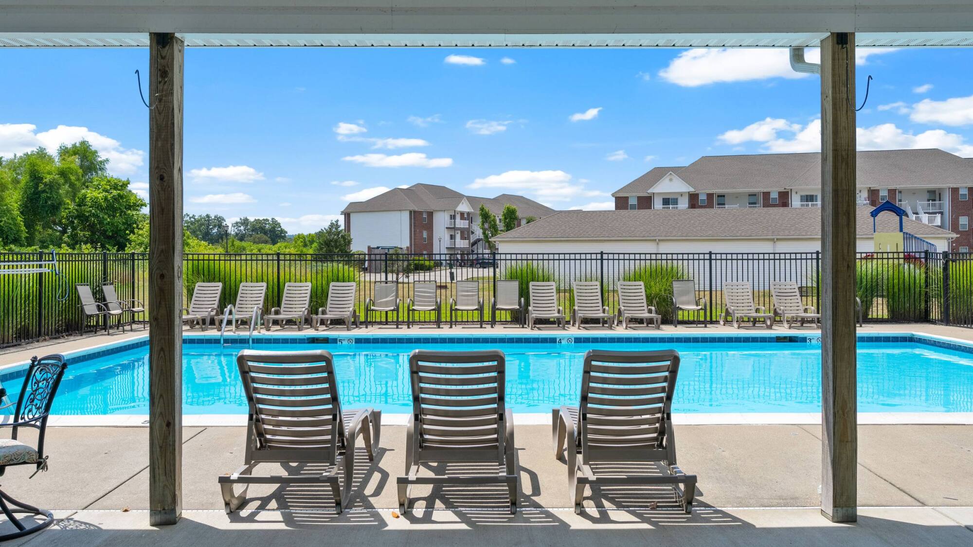 Outdoor pool with lounge chairs around it, apartment buildings and blue sky visible in the background.